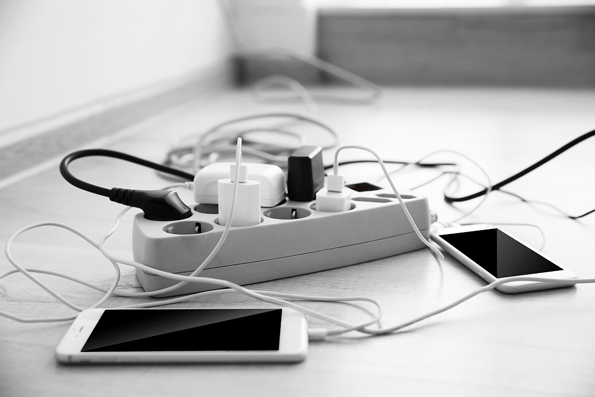 Mobile phones charging into power cord on wooden floor indoors. (Adobe Stock-#108250553 │ Africa Studio)