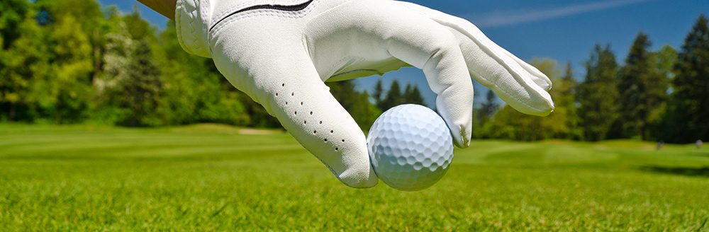 Hand placing golf ball on tee over beautiful golf course with blue sky. (Adobe Stock-#127222431 │ karamysh)