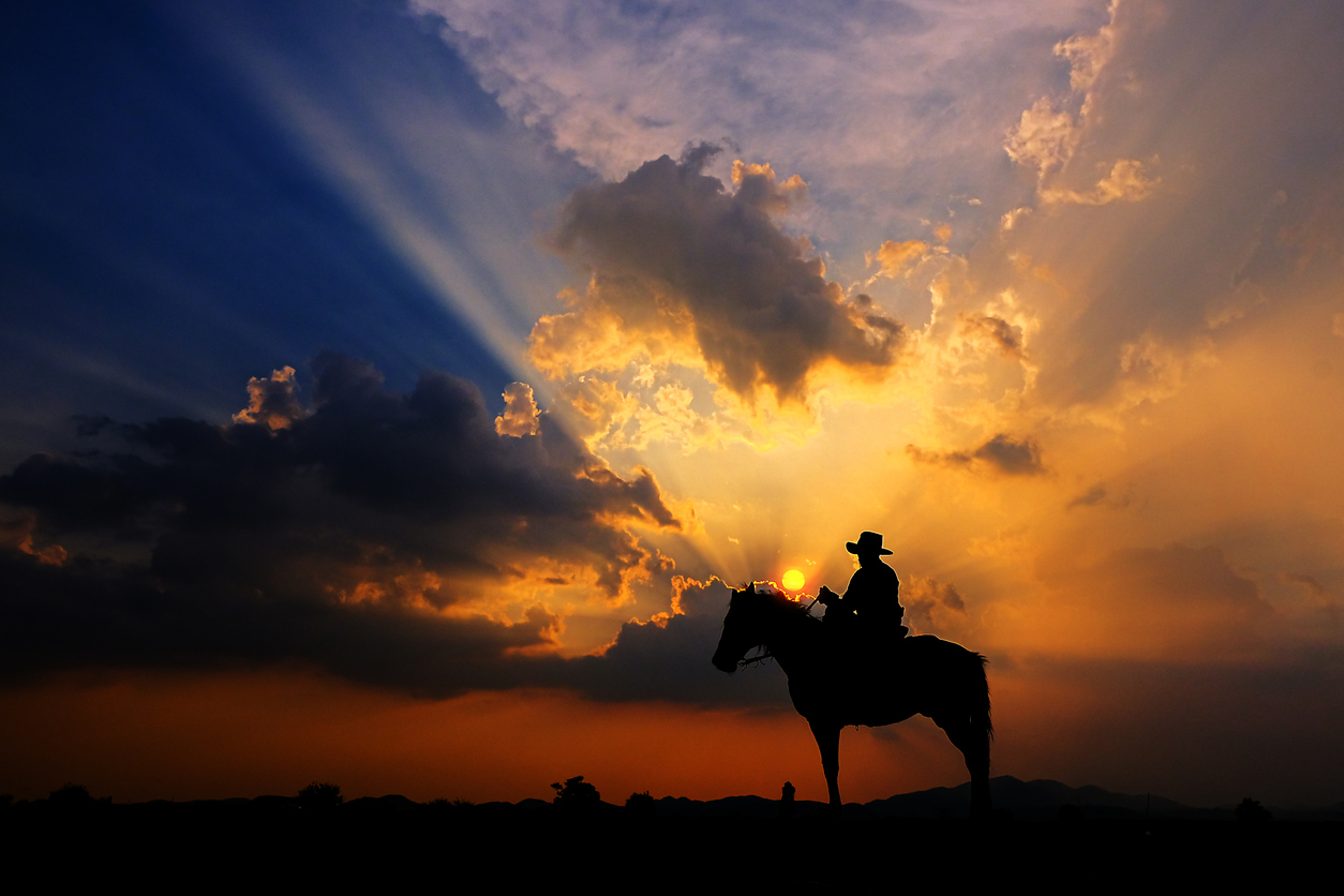 The silhouette of a cowboy on horseback at sunset on a background. (iStock-#1165094937 │ subinpumsom)