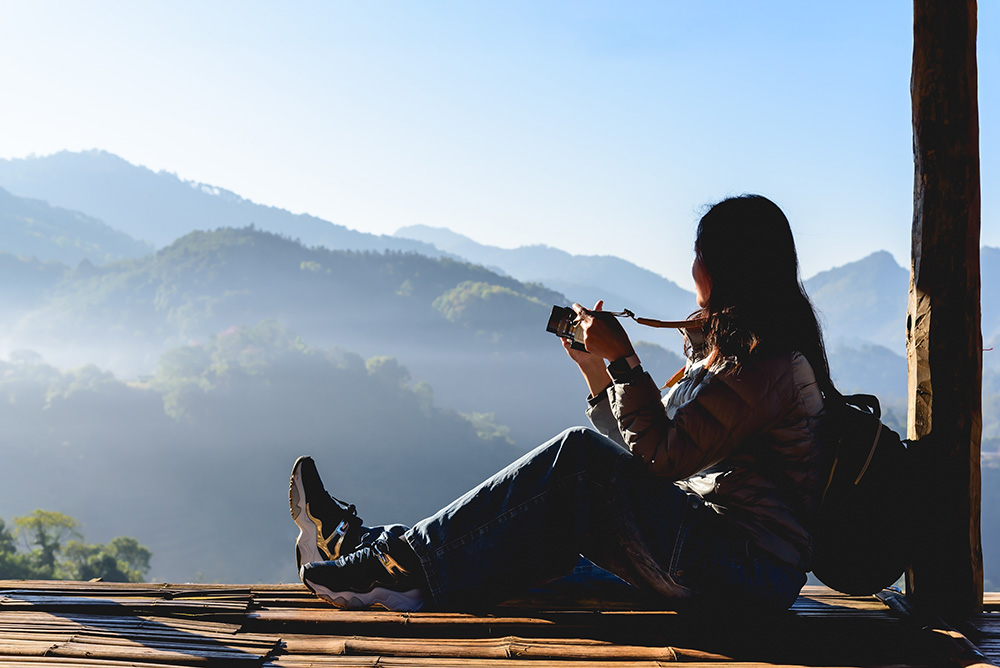 Woman traveler with camera enjoying a mountain view. (Adobe Stock-#1205421233 │ torjrtrx)