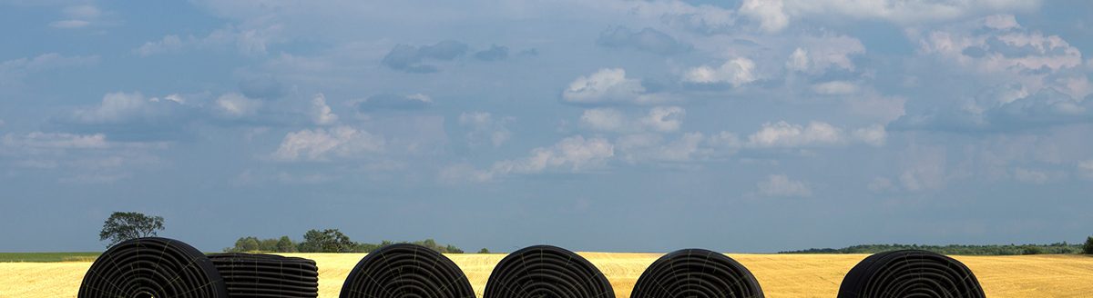 A farm field with rolls of plastic drainage tile in a row ready to be buried in the ground. (iStock-#176447321 │ SimplyCreativePhotography)