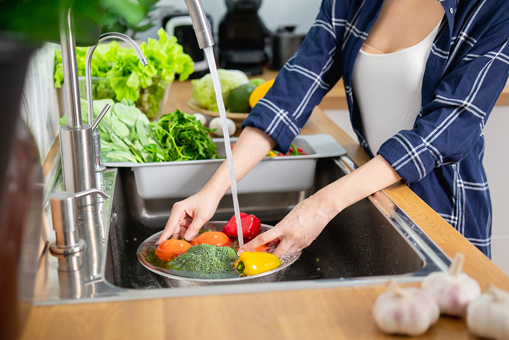 Close up woman washing vegetables above kitchen sink. (Adobe Stock-#470081576 │ khwanchai)