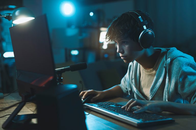Teenager wearing headphones and playing online video games. (Adobe Stock-#478073888 │ stokkete)