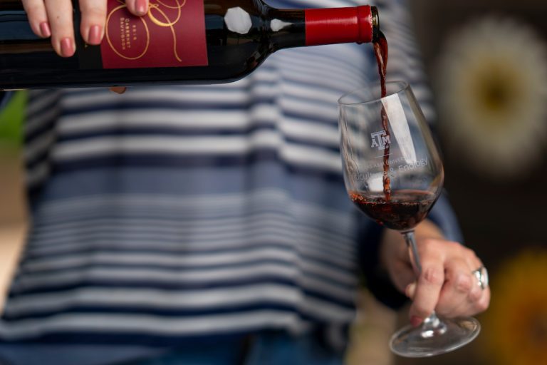 Andreea Botezatu pours wine into a Texas A&M branded glass. (Michael Miller/Texas A&M AgriLife)
