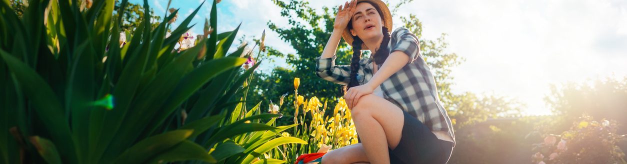 A young woman sits in the garden, wiping the sweat from her brow. (iStock-#1366545439 │ Ildar Abulkhanov)
