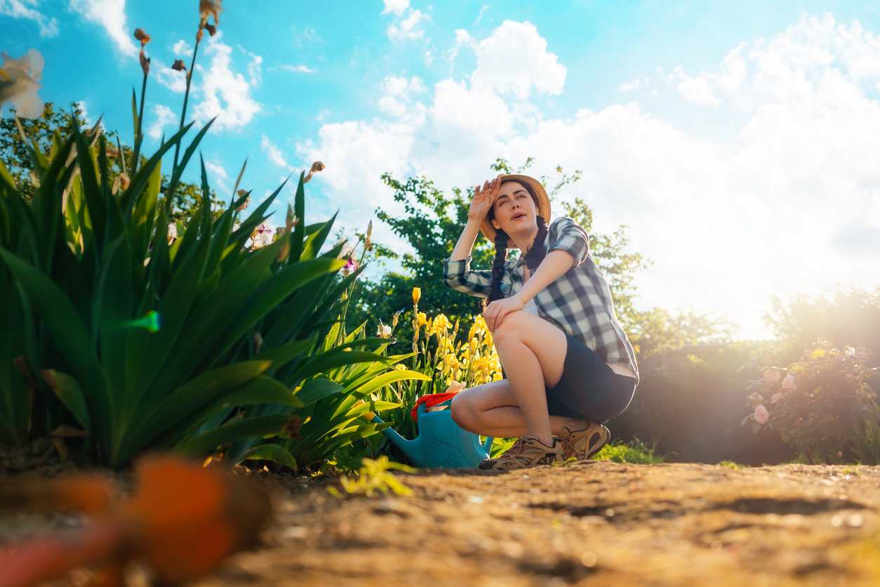 A young woman sits in the garden, wiping the sweat from her brow. (iStock-#1366545439 │ Ildar Abulkhanov)