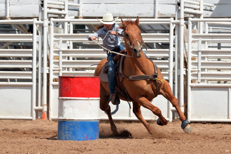 Young girl in western attire riding a horse around a barrel in a race during a rodeo. (iStock-#496662190 │ dgphotography)