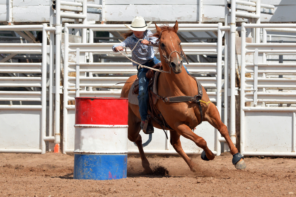 Young girl in western attire riding a horse around a barrel in a race during a rodeo. (iStock-#496662190 │ dgphotography)