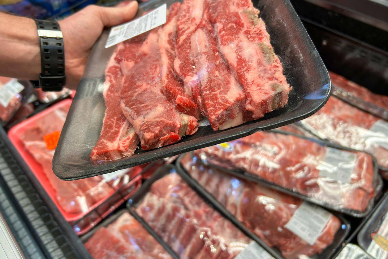A tray of packaged raw beef ribs, with more trays of meat in the background at a grocery store. (iStock-#2160294496 │ nastya_ph)