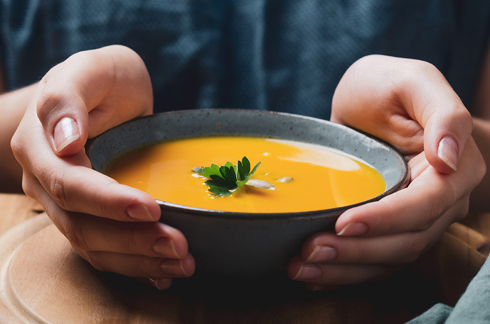 Female hand holding a bowl with pumpkin cream soup. (Adobe Stock-#281375062 │ larionovao)