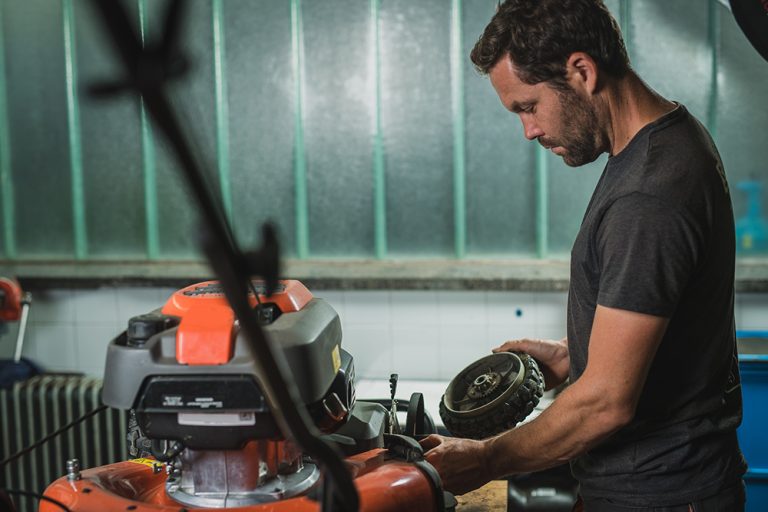 Professional serviceman is repairing a lawnmower, refitting a front wheel. (Adobe Stock-#336308236 │ Anze)